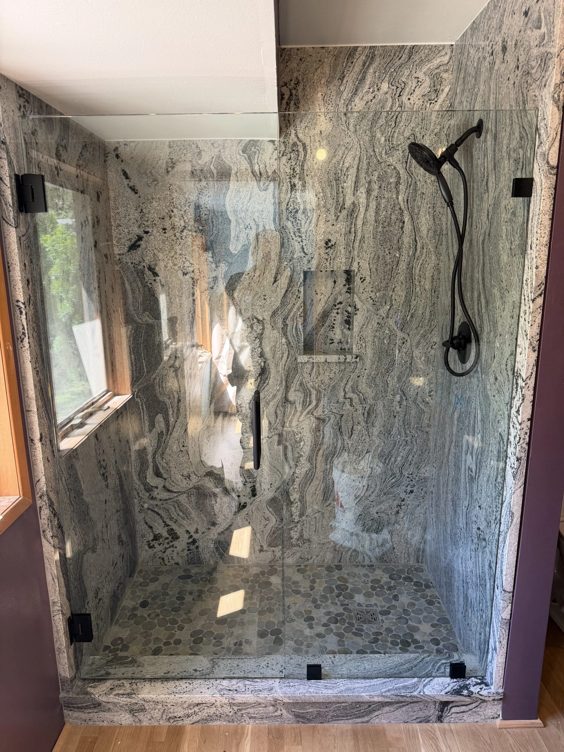 Frameless glass shower with matte black hardware and marble-look walls